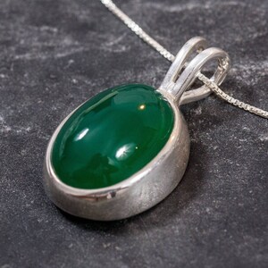 May include: A silver pendant necklace with a green oval gemstone. The pendant is set in a silver bezel and hangs from a delicate silver chain.