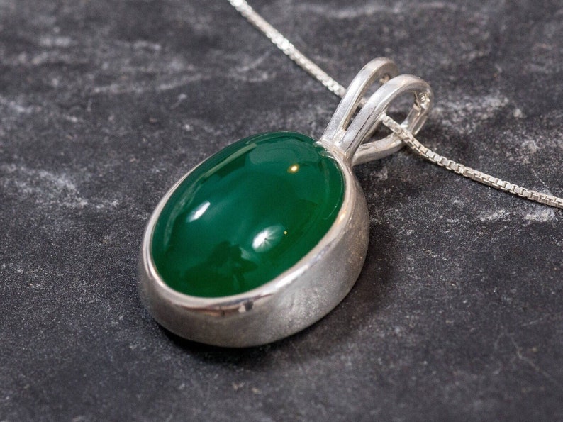 May include: A silver pendant necklace with a green oval gemstone. The pendant is set in a silver bezel and hangs from a delicate silver chain.