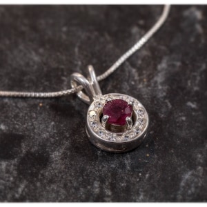 May include: A silver necklace with a pendant featuring a red gemstone surrounded by smaller white gemstones.