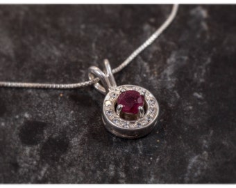 Puede incluir: Un collar de plata con un colgante que presenta una piedra roja rodeada de piedras blancas más pequeñas.