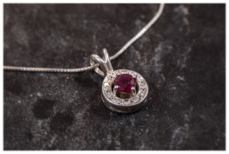 May include: A silver necklace with a pendant featuring a red gemstone surrounded by smaller white gemstones.