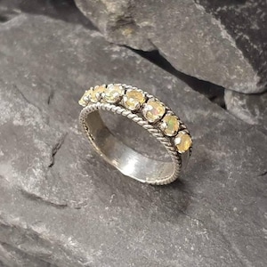 Puede incluir: Un anillo de banda de plata con una fila de peque&ntilde;os &oacute;palos blancos redondos engastados en un dise&ntilde;o de cuerda.