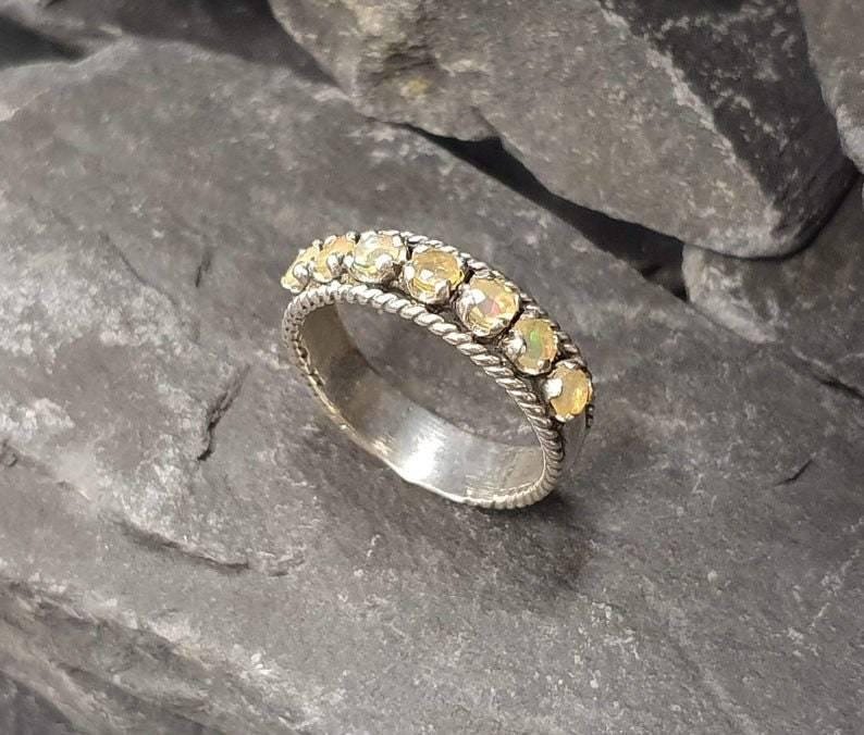 Puede incluir: Un anillo de banda de plata con una fila de peque&ntilde;os &oacute;palos blancos redondos engastados en un dise&ntilde;o de cuerda.
