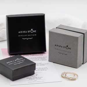 Puede incluir: Tres cajas de joyer&iacute;a negras con el texto "Adina Stone Jewelry Boutique" en la parte superior. Las cajas est&aacute;n sobre una superficie blanca con una tarjeta rosa y blanca que dice "Made with Love Adina Stone".