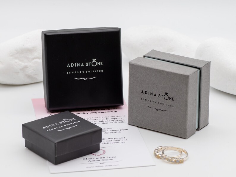 Puede incluir: Tres cajas de joyer&iacute;a negras con el texto "Adina Stone Jewelry Boutique" en la parte superior. Las cajas est&aacute;n sobre una superficie blanca con una tarjeta rosa y blanca que dice "Made with Love Adina Stone".