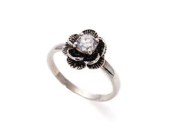 Peut inclure: Une bague en argent avec un strass clair serti dans un motif de fleur noire.