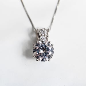 May include: A silver necklace with a large, clear, round pendant featuring a smaller clear stone on each side.
