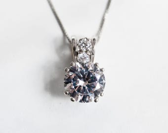 May include: A silver necklace with a large, clear, round pendant featuring a smaller clear stone on each side.