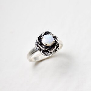 Op de afbeelding: Een zilveren ring met een witte opaal in een bloemvorm.