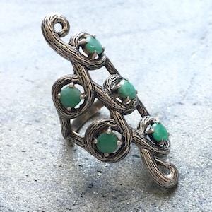 May include: A silver ring with a unique design featuring four green gemstones set in a twisted branch-like pattern.
