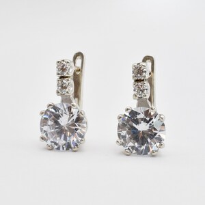 May include: A pair of silver earrings with a large round clear crystal and two smaller clear crystals on the top of the earring.