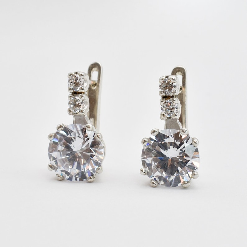 May include: A pair of silver earrings with a large round clear crystal and two smaller clear crystals on the top of the earring.