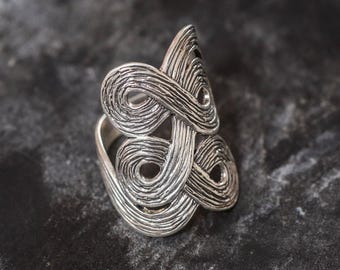 Könnte beinhalten: Ein silberner Ring mit einem strukturierten, abstrakten Design. Der Ring besteht aus einem einzigen Stück Metall, das verdreht und gewendet wird, um ein einzigartiges und kompliziertes Muster zu schaffen.