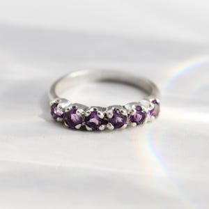 Könnte beinhalten: Ein Silberring mit einer Reihe von sieben violetten Amethyststeinen.