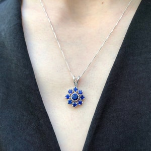 May include: A silver necklace with a pendant featuring a cluster of blue gemstones in a flower shape.