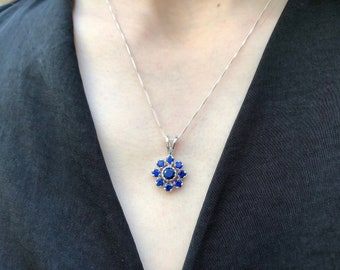 Pode incluir: Um colar de prata com um pingente em forma de flor com um grupo de pedras preciosas azuis.
