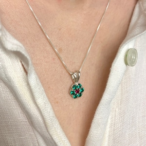 Könnte beinhalten: Eine silberne Kettenkette mit einem kleinen Anhänger in Form einer roten und grünen Blume.