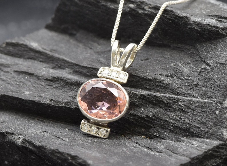 May include: A silver chain necklace with a pink oval gemstone pendant accented with small clear gemstones.
