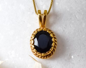 Pode incluir: Um colar de corrente de ouro com um pingente oval de pedra preta. O pingente tem uma borda dourada com um design decorativo.