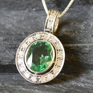 May include: A silver pendant necklace with a large oval green gemstone surrounded by a halo of smaller diamonds.