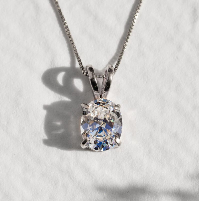 May include: A silver chain necklace with a round, clear, faceted gemstone pendant.