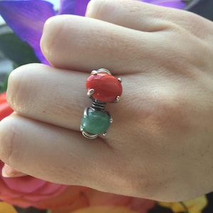 May include: A silver ring with two oval-shaped gemstones. The top stone is red and the bottom stone is green.