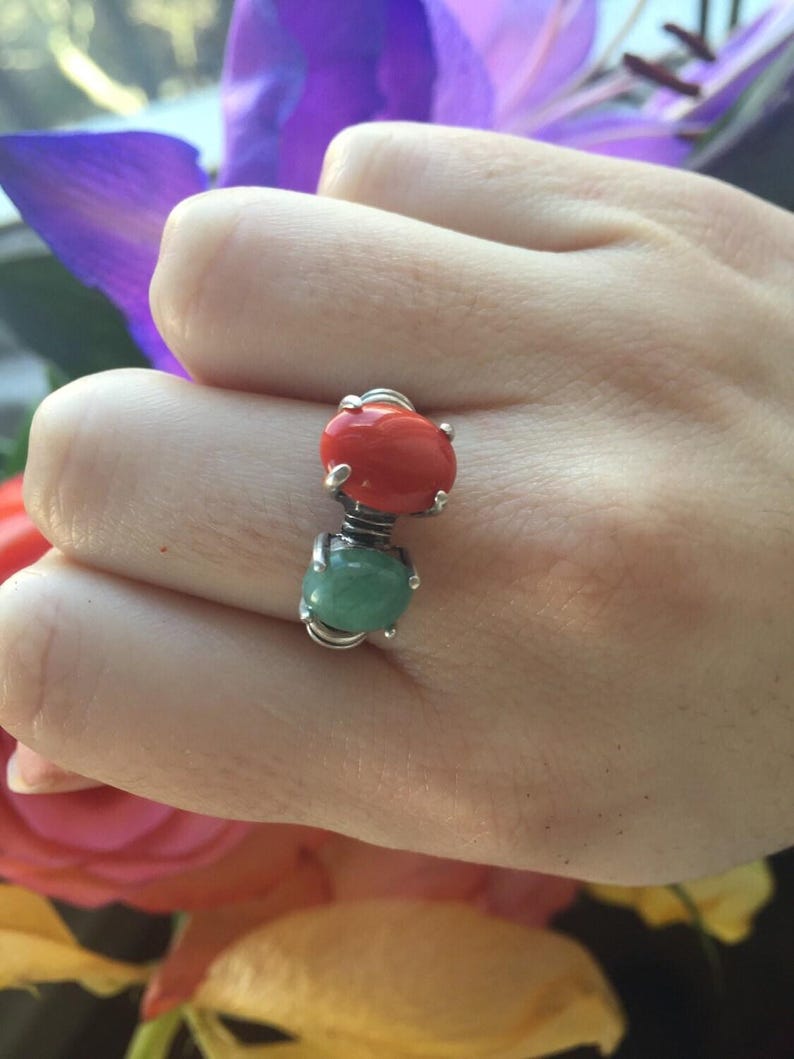 May include: A silver ring with two oval-shaped gemstones. The top stone is red and the bottom stone is green.