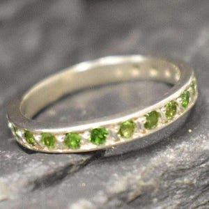 以下が含まれることがあります： バンドに緑色の宝石が並んだシルバーのリングです。