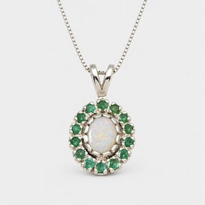 May include: A silver pendant necklace featuring a central oval-shaped iridescent opal surrounded by a halo of small, round, vibrant green emerald gemstones. The pendant hangs from a delicate silver chain with a classic box link design.