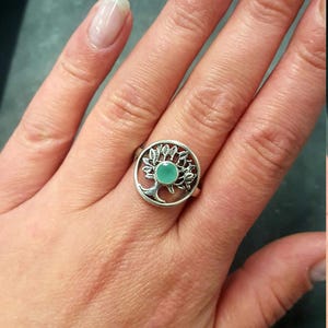 May include: A silver ring with a tree design and a light green gemstone in the center.