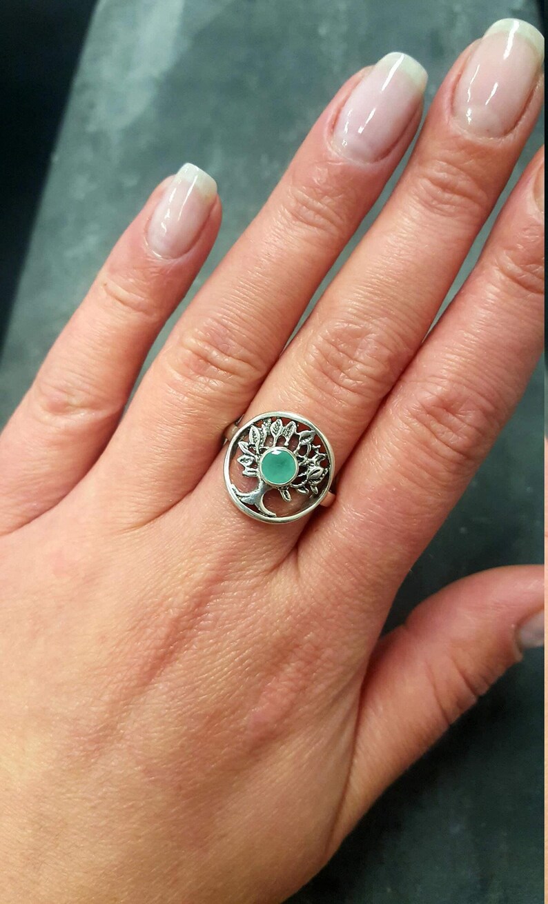 May include: A silver ring with a tree design and a light green gemstone in the center.