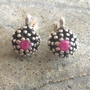 May include: A pair of silver earrings with pink gemstone accents. The earrings have a textured, floral design.