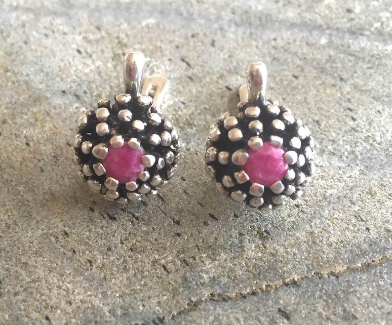 May include: A pair of silver earrings with pink gemstone accents. The earrings have a textured, floral design.