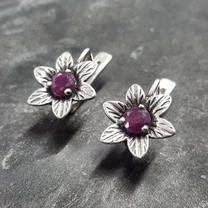 May include: A pair of silver flower-shaped earrings with pink gemstones in the center.