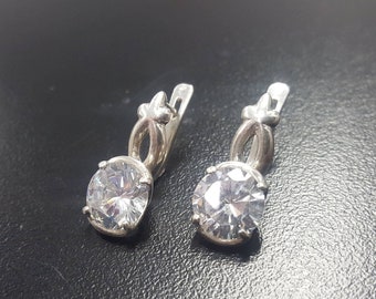 May include: A pair of silver earrings with a clear round stone and a delicate floral design.