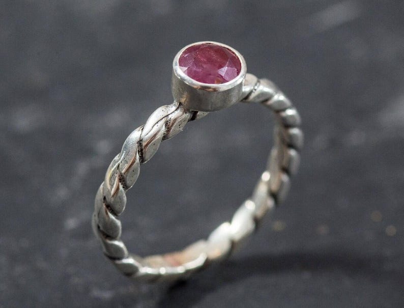 Puede incluir: Un anillo de plata con una banda trenzada y una piedra preciosa rosa.