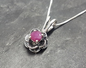 May include: A silver necklace with a pink ruby gemstone set in a flower-shaped pendant.