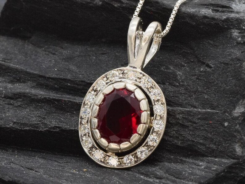 May include: A silver pendant necklace with a red oval gemstone surrounded by a halo of smaller white gemstones.
