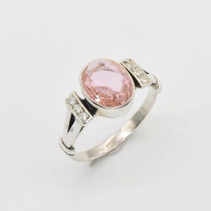 May include: A silver ring with a pink oval gemstone and small diamonds on the band.