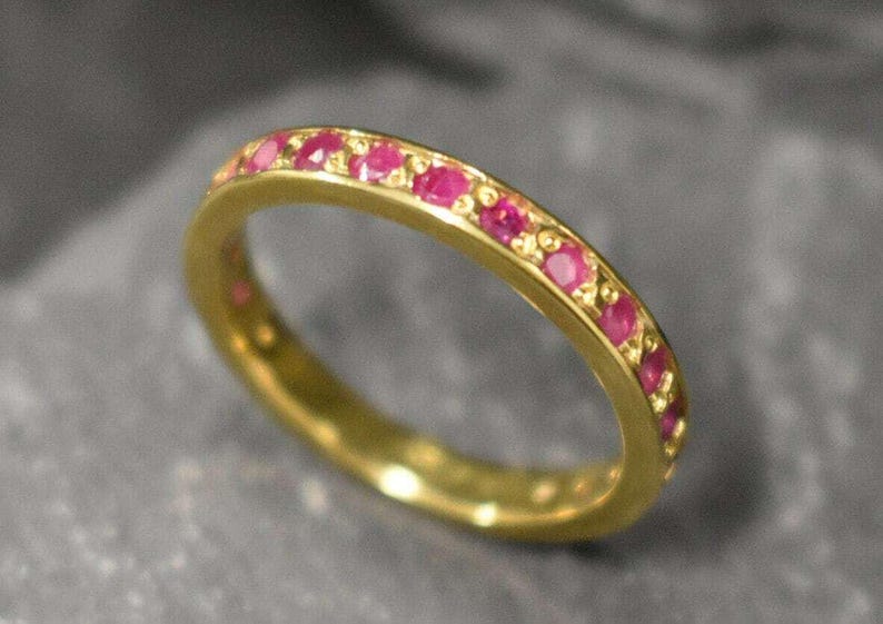 Puede incluir: Un anillo de banda de oro con una fila de peque&ntilde;as piedras de rub&iacute; rosa engastadas en la banda.
