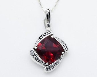 May include: A silver pendant necklace featuring a red gemstone set in a square design. The pendant has intricate details and a delicate chain.