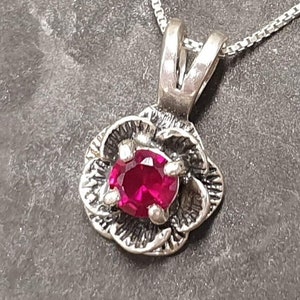 Peut inclure: Un collier avec un pendentif en argent en forme de fleur avec une pierre précieuse rose.