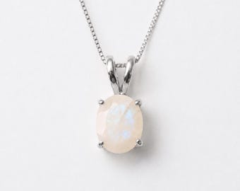 Può includere: Una collana d'argento con un pendente ovale, iridescente, bianco sporco. Il pendente è tenuto da un'ansa d'argento e ha una sottile lucentezza perlacea. La catena è una delicata catena d'argento.