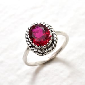 May include: A silver ring with a red oval gemstone set in a rope-like design.