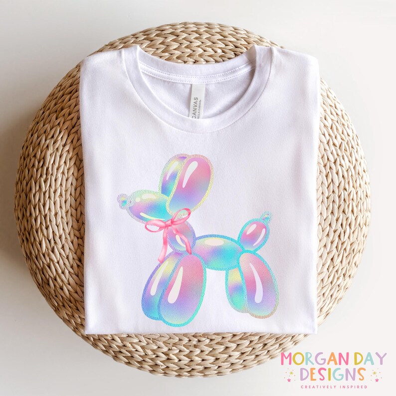 May include: White t-shirt with a colorful balloon animal design. The balloon animal is a dog with iridescent colors and a pink ribbon.