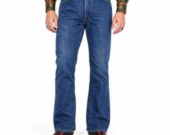May include: Medium-wash blue denim jeans featuring a classic five-pocket design, a button fly closure, and a straight-leg cut. The denim has a consistent blue tone with subtle fading along the thighs and knees, finished with copper-colored rivets.