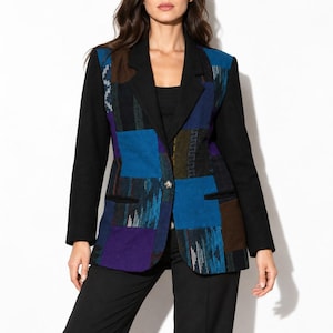May include: A blazer featuring a patchwork design with solid black sleeves and lapels. The front panels display a mix of blue, purple, and brown textured fabric squares with varied patterns. The garment includes two front pockets and a single button closure.