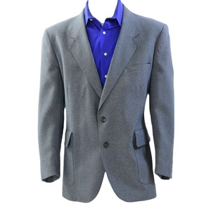 May include: A gray blazer with a blue dress shirt underneath. The blazer has two buttons and two front pockets. The dress shirt has a button-down collar.