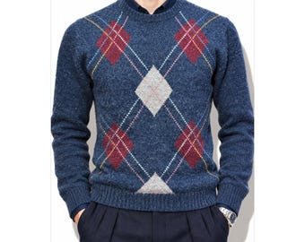 May include: A blue crew neck sweater featuring a textured knit finish and an argyle pattern composed of red and light gray diamonds outlined with thin white and yellow lines, worn over a dark blue collared shirt and dark trousers.