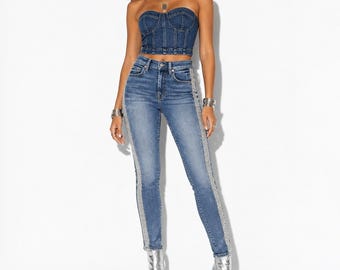 May include: A dark blue denim strapless corset top with visible stitching and matching high-waisted skinny jeans featuring a vertical silver sequin or rhinestone stripe running down the outer side of each leg, paired with metallic silver ankle boots.